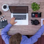 Screenwriter working on his laptop and taking hand written notes at the same time.